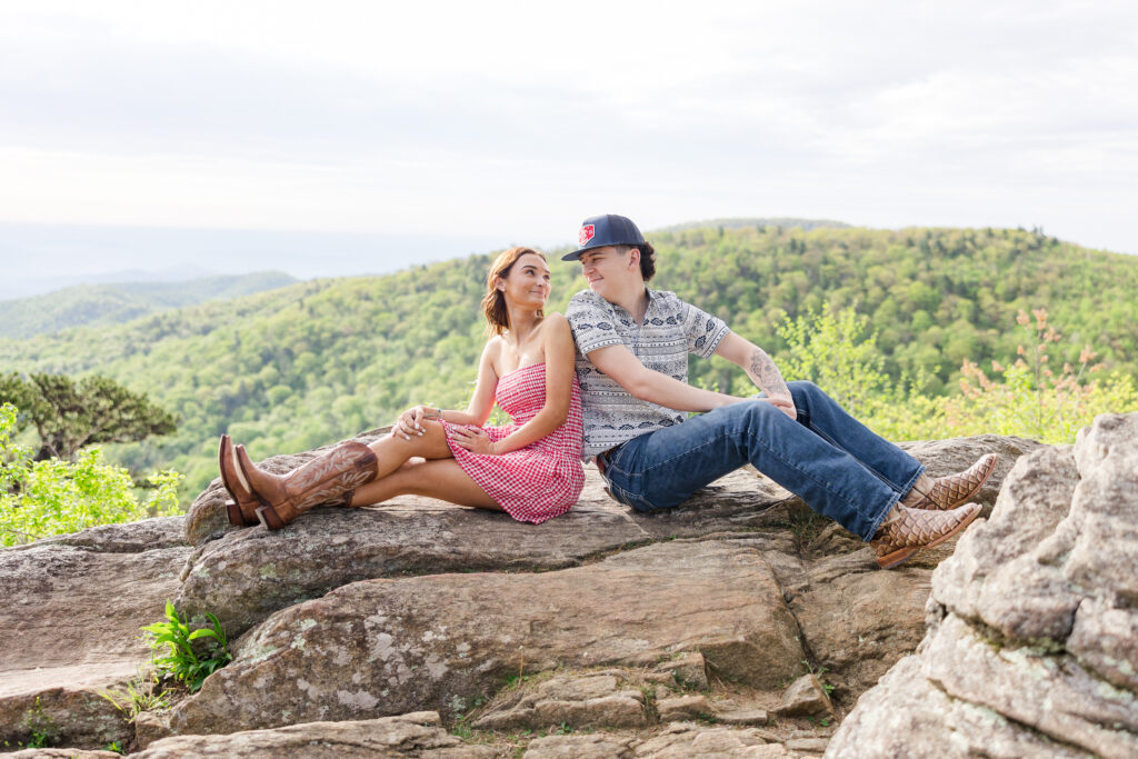 couple on a rock smiling at each other at an overlook at Shenandoah National Park